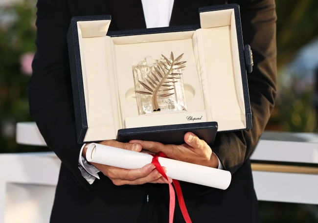 Person holding the Cannes Film Festival Palme d’Or trophy in its case with a red-tied certificate.